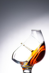 a drop falling into a glass with a broken wall with cognac or whiskey, a splash at an amazing angle