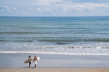 couple surfer walking toward the sea while holding surfing  board