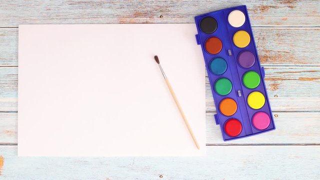 Painting tools, watercolors and drawing block appear on wooden table - Stop motion