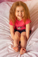 Caucasian little girl with lush hair laughing while sitting on bed