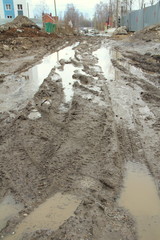 Dirty dirt road with track, wheel marks, brown clay and puddles in Russia.