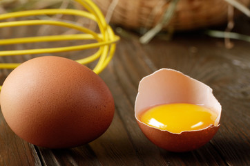 Raw organic brown chicken broken eggs with yolk wicker basket and whisk on kitchen wooden table
