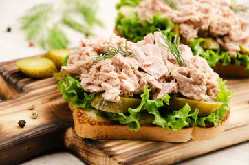 Homemade tuna salad sandwiches on cutting board with pickles aside