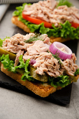 Tuna sandwiches with lettuce tomatoes pickles and onions on slate tray