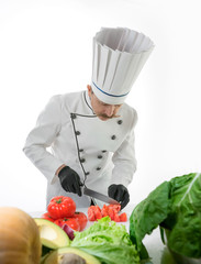 Chef cook cut tomatoes with a knife at the white table with a vegetables