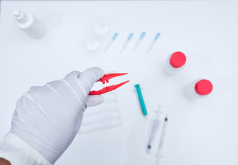 Doctor wearing gloves holding a pair of tweezers in a white background with medical instrument.Laboratory test,research,technology
