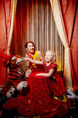 Obraz na płótnie Canvas Family during a stylized theatrical circus photo shoot in a beautiful red location. Models mother and daughter posing on stage with curtain