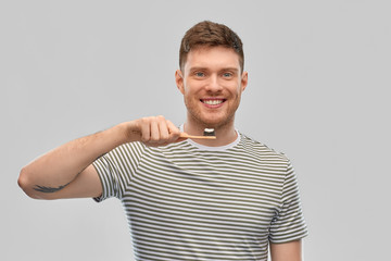 Fototapeta premium dental care, oral hygiene and people concept - happy smiling young man with toothpaste on wooden toothbrush over gray background