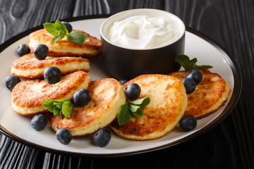 Recipe for delicious cottage cheese syrniki served with blueberries, mint and sour cream close-up in a plate. horizontal