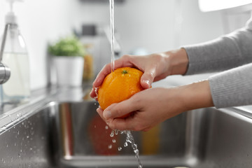 hygiene, health care and safety concept - close up of woman's hands washing orange fruit in kitchen at home