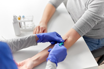 medicine, healthcare and diabetes concept - close up of doctor in gloves with syringe taking blood for test from patient's hand at hospital
