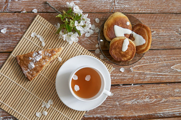 Pile of small homemade pancakes with honey, tea cup and honeycomb on wooden table