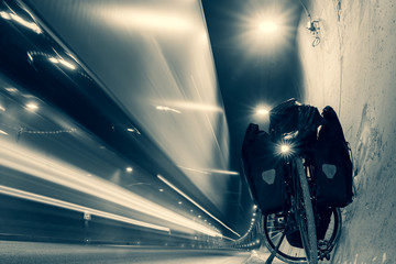 Touring bicycle is standing on the side inside the tunnel with cars passing by. Safety and dangers of bicycle travel. Black and white background.