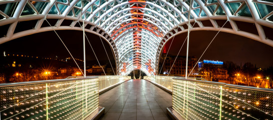 Panoramic image of architecture and pathway of iliuminated Peace bridge in Tblisi at night time....