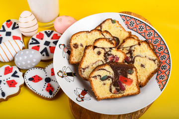 Slices of Romanian sponge cake or chec, cozonac with red traditional towel with manual stitch on wooden board, Easter painted eggs and home made ginger bread hearts, Authentic Easter Brunch concept. 