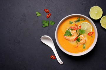 Tom Yam kung Spicy Thai soup with shrimp, coconut milk and chili pepper in bowl. Black stone background