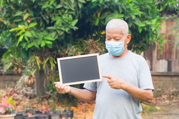 Portrait of senior man standing holding a black label and wearing face mask for healthy because have air pollution PM 2.5. Mask for protect Virus, Bacteria, Pollen Grains. Healthcare concept