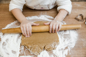 Baby girl is preparing in kitchen.View from above.Little hands with rolling pin,dought and flour on the wooden table.