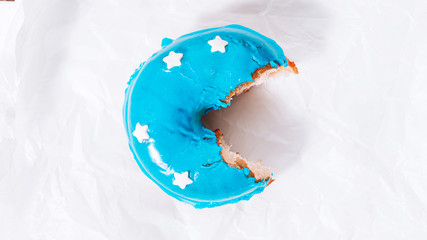 a donut with blue icing and white stars on white paper with a bitten bite