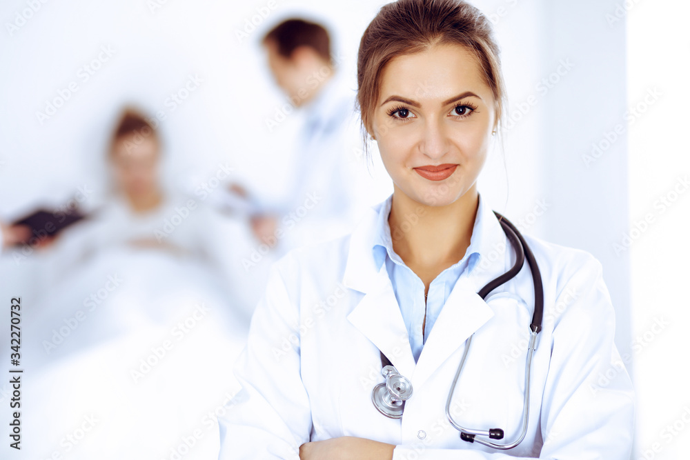 Wall mural Female doctor smiling on the background with patient in the bed and two doctors