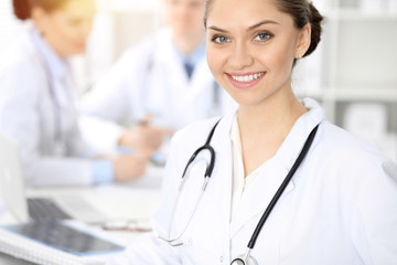 Happy smiling woman-doctor sitting and looking at camera at meeting with medical staff . Medicine concept