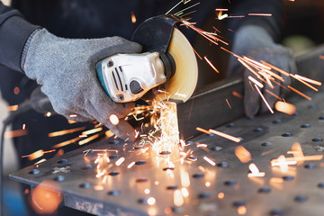 A metal worker cuts a rectangular metal pipe with an angle grinder - obrazy, fototapety, plakaty