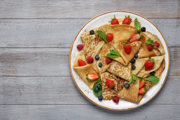 Thin crepes decorated with fresh berries and mint leaves. Traditional Russian, Ukrainian or French pancakes