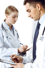 Obraz premium Doctors writing papers using clipboard. Physicians discussing medication program or studying at medical conference. Healthcare, insurance and medicine concept