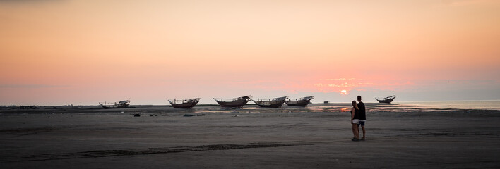 Masirah Island, Oman, December 31, 2019: beautiful panoramic image of a loving couple taking a walk on the beach with boats stranded in the background during sunset