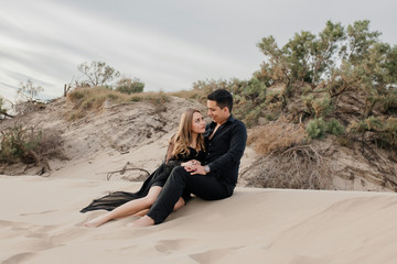 Fototapeta premium Attractive couple in playful love sitting on the sand holding each other Black formal shirt and pants