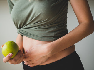 Beautiful sporty woman holds a green apple in hand near waistline. Healthy food