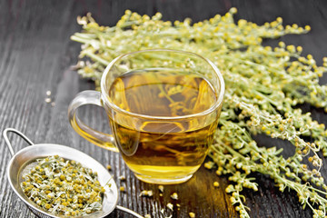 Tea of gray wormwood in glass cup with strainer on wooden board