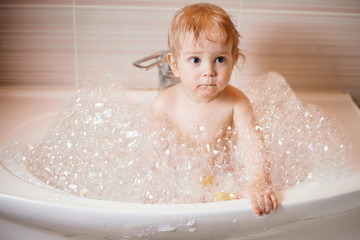 Funny child playing with water and foam in a bathroom.