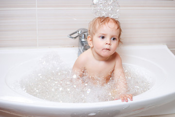 Funny child playing with water and foam in a bathroom.