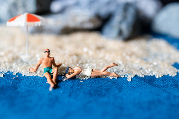 Miniature people wearing swimsuit relaxing on the beach with blue background , Summer time concept
