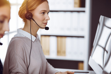 Businesswoman talking by headset in sunny office. Call center and diverse people group in business