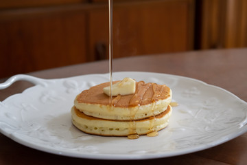 自宅で手作りしたパンケーキ　お皿に盛り付けたパンケーキにメープルシロップをかける様子