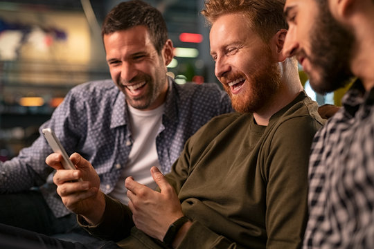 Friends laughing and using smartphone at pub - Powered by Adobe