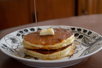 自宅で手作りしたパンケーキ　お皿に盛り付けたパンケーキにメープルシロップをかける様子