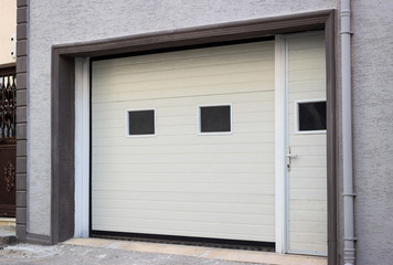 White garage door in grey apartment building. PVC door in new building.