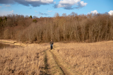A man rides a Bicycle on dry grass against a background of bare trees.