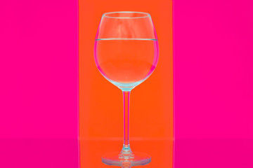 transparent glasses with clear water on Coloured various background with striped optical reflections. Reflected on a mirror on a red and yellow background
