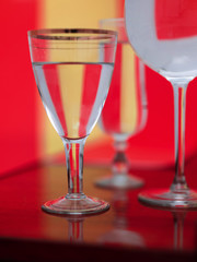 transparent glasses with clear water on Coloured various background with striped optical reflections. Reflected on a mirror on a red and yellow background