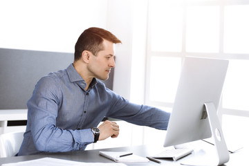 Fototapeta premium Businessman working with computer in modern sunny office. Headshot of male entrepreneur or company director at workplace. Business concept