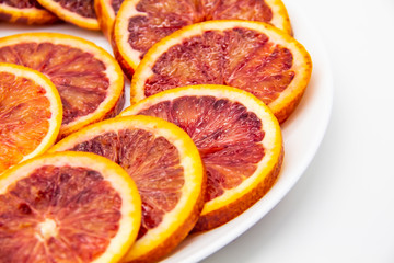 Sicilian sliced ​​orange on a white plate on a white background. Sliced ripe Sicilian oranges against background. Healthy and tasty red sliced ​​orange