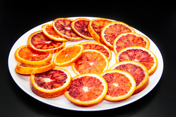 Fototapeta na wymiar Sicilian sliced ​​orange on a white plate on a dark background. Sliced ripe Sicilian oranges against background. Healthy and tasty red sliced ​​orange.
