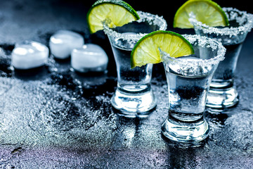 Tequila shot with lime slices and salt on dark background
