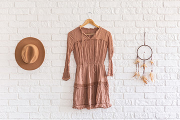 Fashion woman summer dress, hat and dream catcher hanging on white brick wall background. beautiful set clothes hanging on a hanger on a brick wall in a loft studio. Nobody. Showroom - 342283569