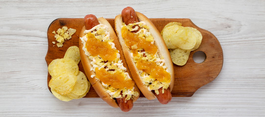 Homemade colombian hot dogs with pineapple sauce, chips and mayo ketchup on a rustic wooden board on a white wooden background, top view. Overhead, flat lay, from above. Close-up.