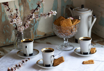 Coffee served with shortbread cookies and sweets on the background of flowering branches and an old cupboard.